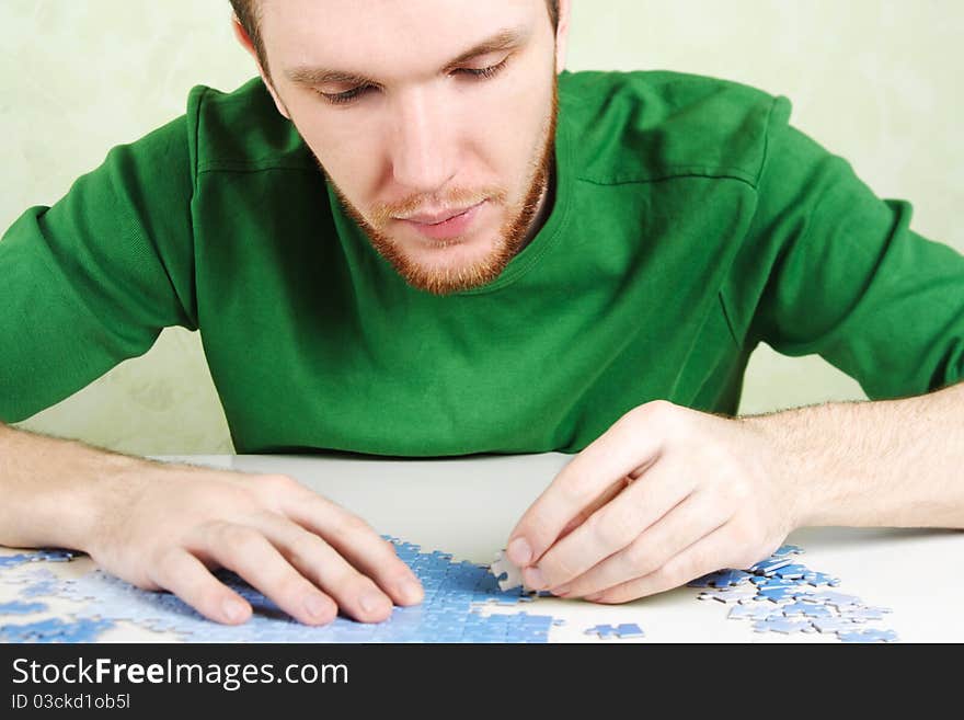 Man in green shirt assembling blue puzzle pieces. Man in green shirt assembling blue puzzle pieces