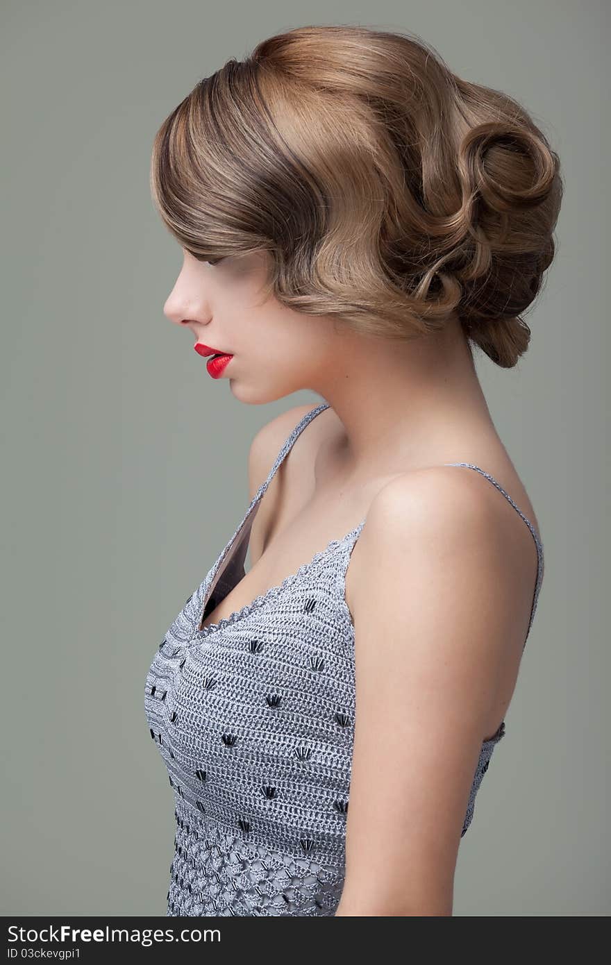 A fashion, beauty, profile photo of a young, blonde woman dressed in an elegant gray dress. she wears bright red lips and black eyeliner. A fashion, beauty, profile photo of a young, blonde woman dressed in an elegant gray dress. she wears bright red lips and black eyeliner.