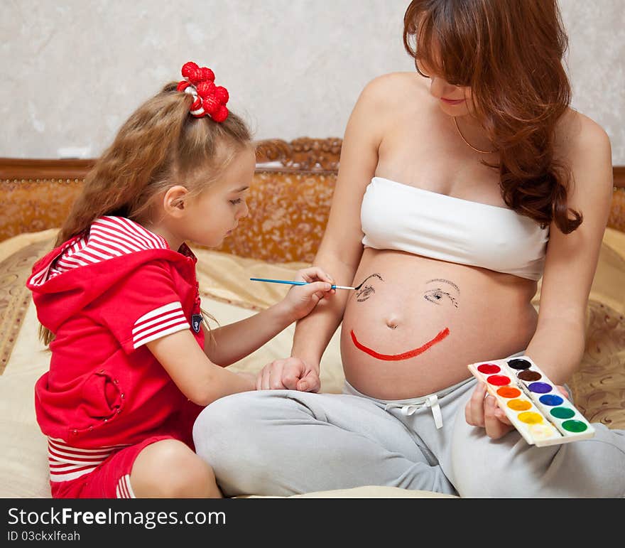 A daughter is painting on he rpregnant mother`s belly. A daughter is painting on he rpregnant mother`s belly