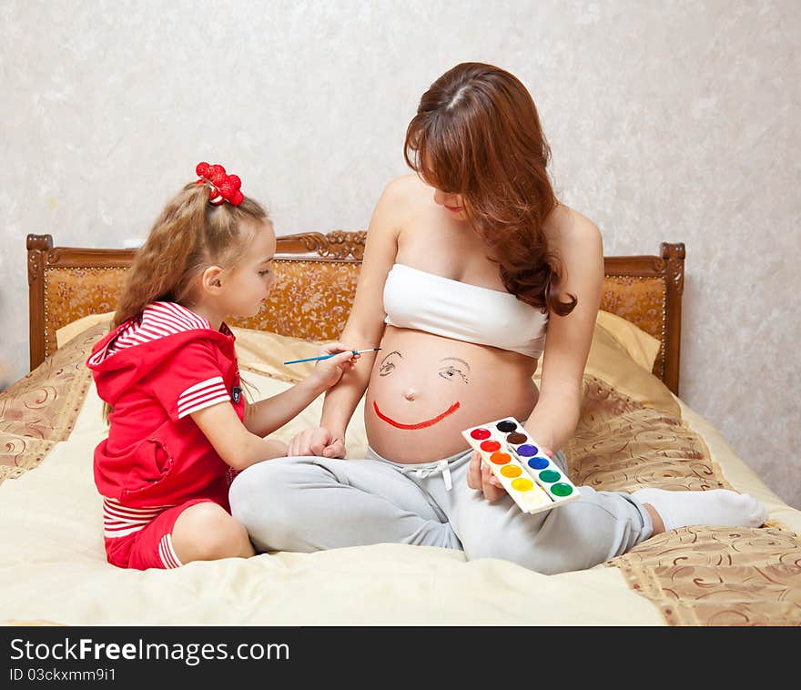 A daughter is painting on he rpregnant mother`s belly. A daughter is painting on he rpregnant mother`s belly