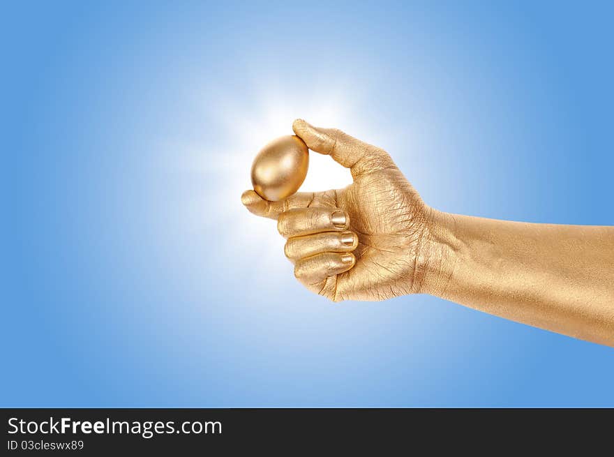 Gold egg in a gold man's hand against the blue sky