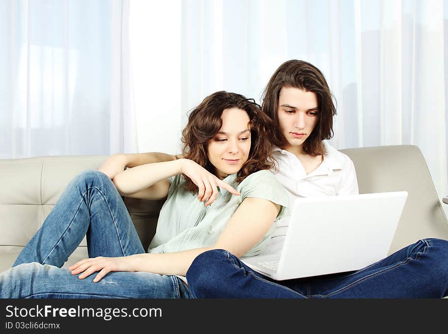 An attractive young couple sitting on a couch together and holding a laptop. They are smiling directly at the camera. An attractive young couple sitting on a couch together and holding a laptop. They are smiling directly at the camera.