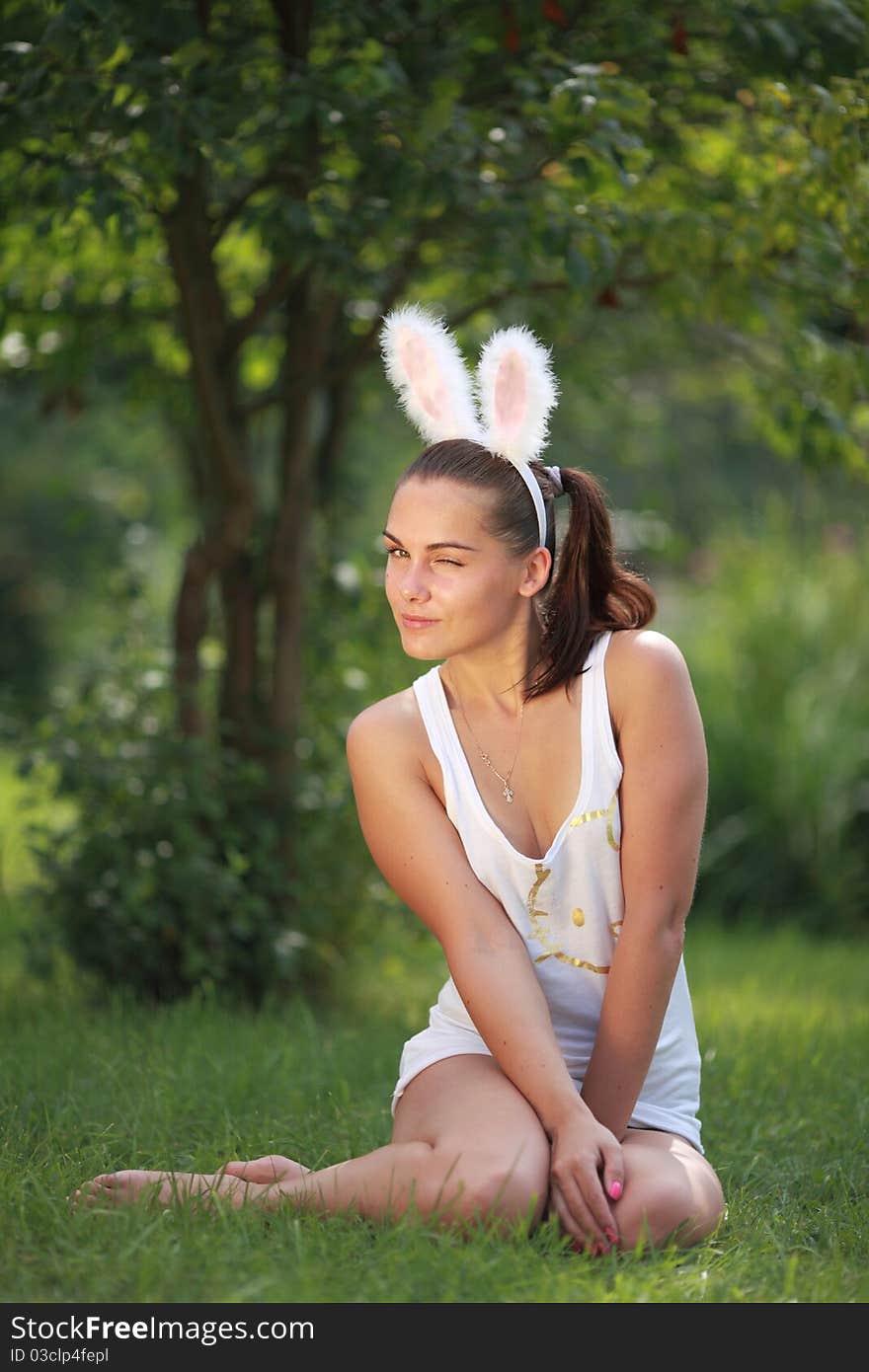 Woman with funny rabbit ears sits on a grass outdoors