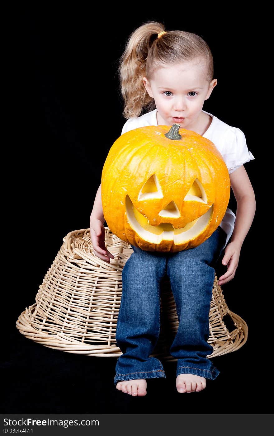 An adorable girl holding a pumpkin on her lap. She is itting on a harvest basket. An adorable girl holding a pumpkin on her lap. She is itting on a harvest basket.