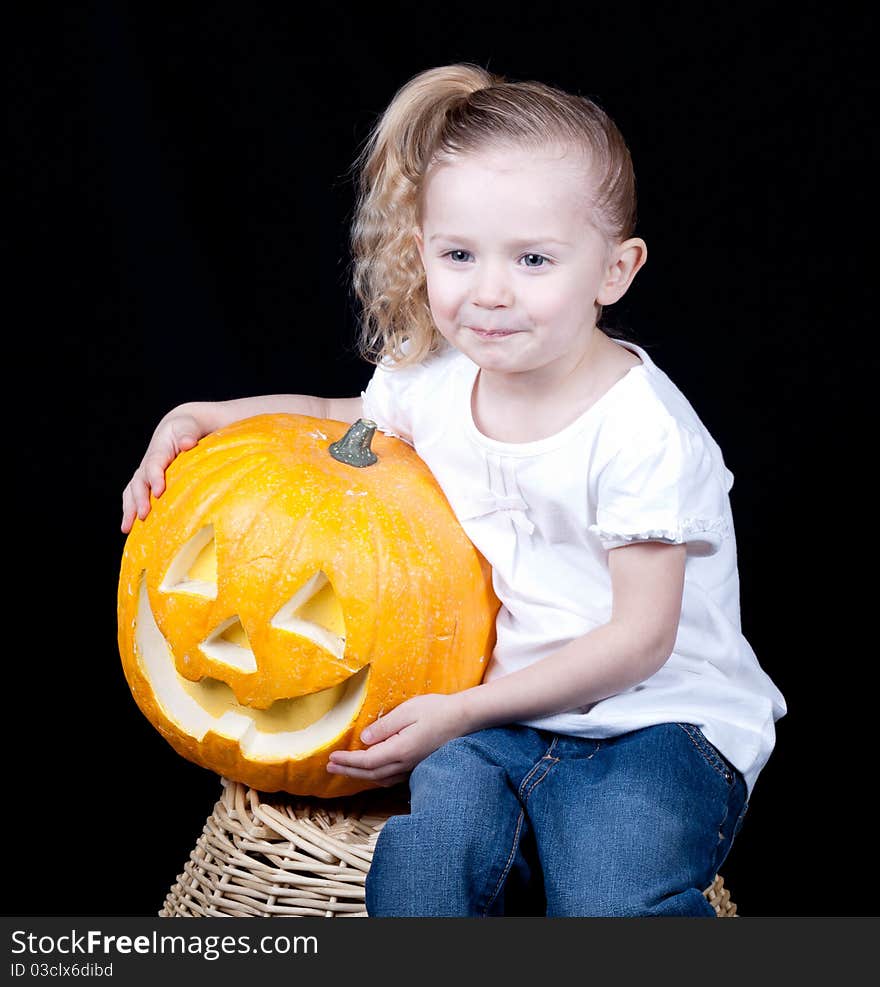 A girl is sitting on a harvest basket holding her pumpkin. A girl is sitting on a harvest basket holding her pumpkin.