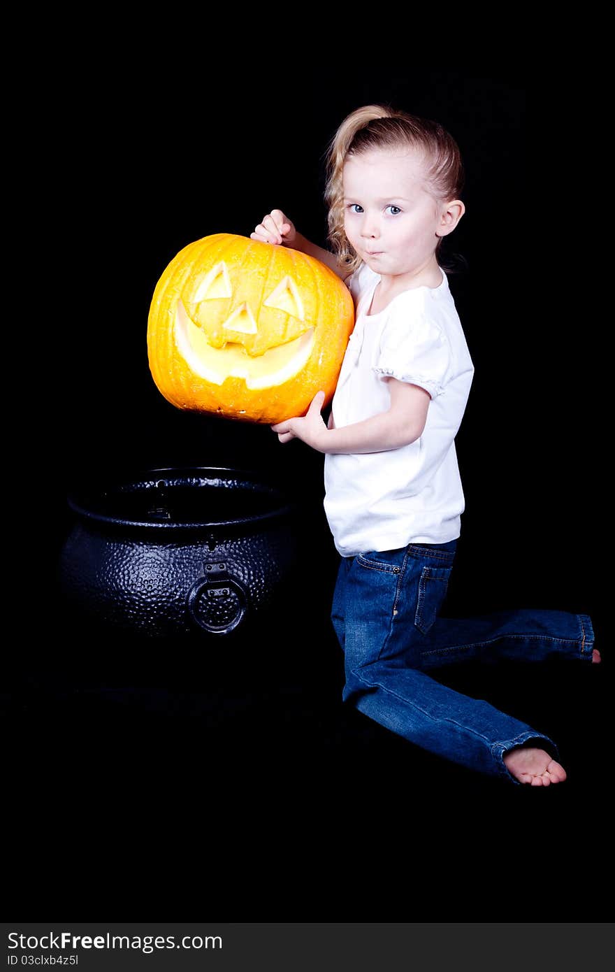 A young girl is trying to make pumpkin pie with a pumpkin and a witches cauldron.