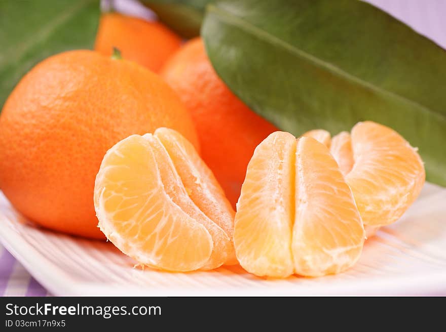 Whole and sectioned clementines over a white dish. Selective focus, extra-shallow DOF.