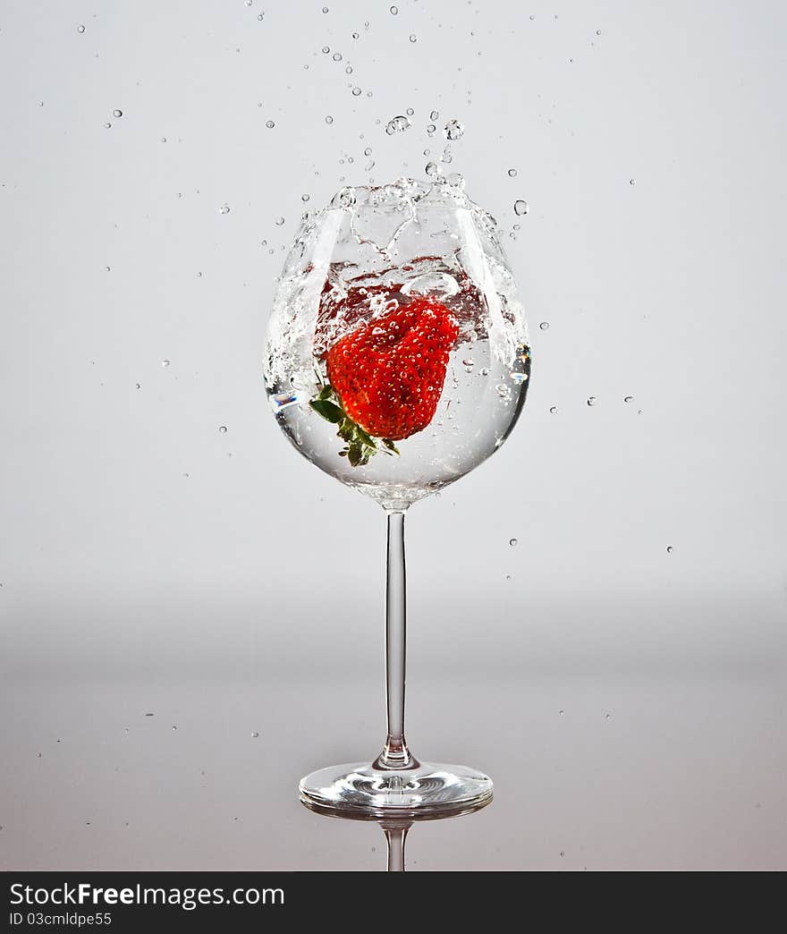 One red strawberry fallen into a glass of water. One red strawberry fallen into a glass of water