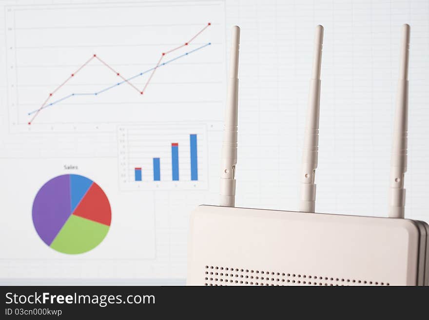 Wireless business concept with router on foreground and busines diagrams on background. Focus on router