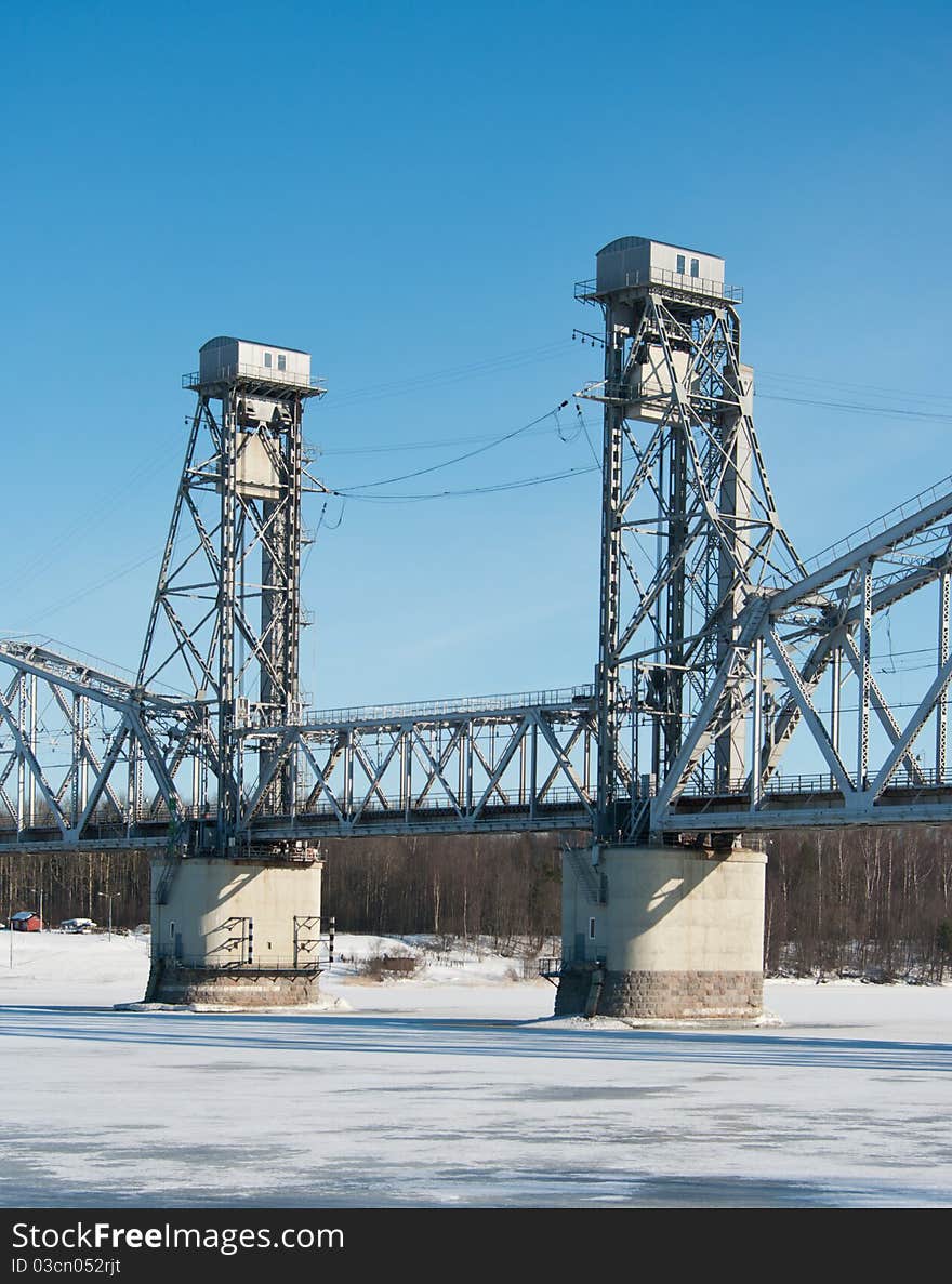 Railroad bridge across the frozen river on the background of blue sky