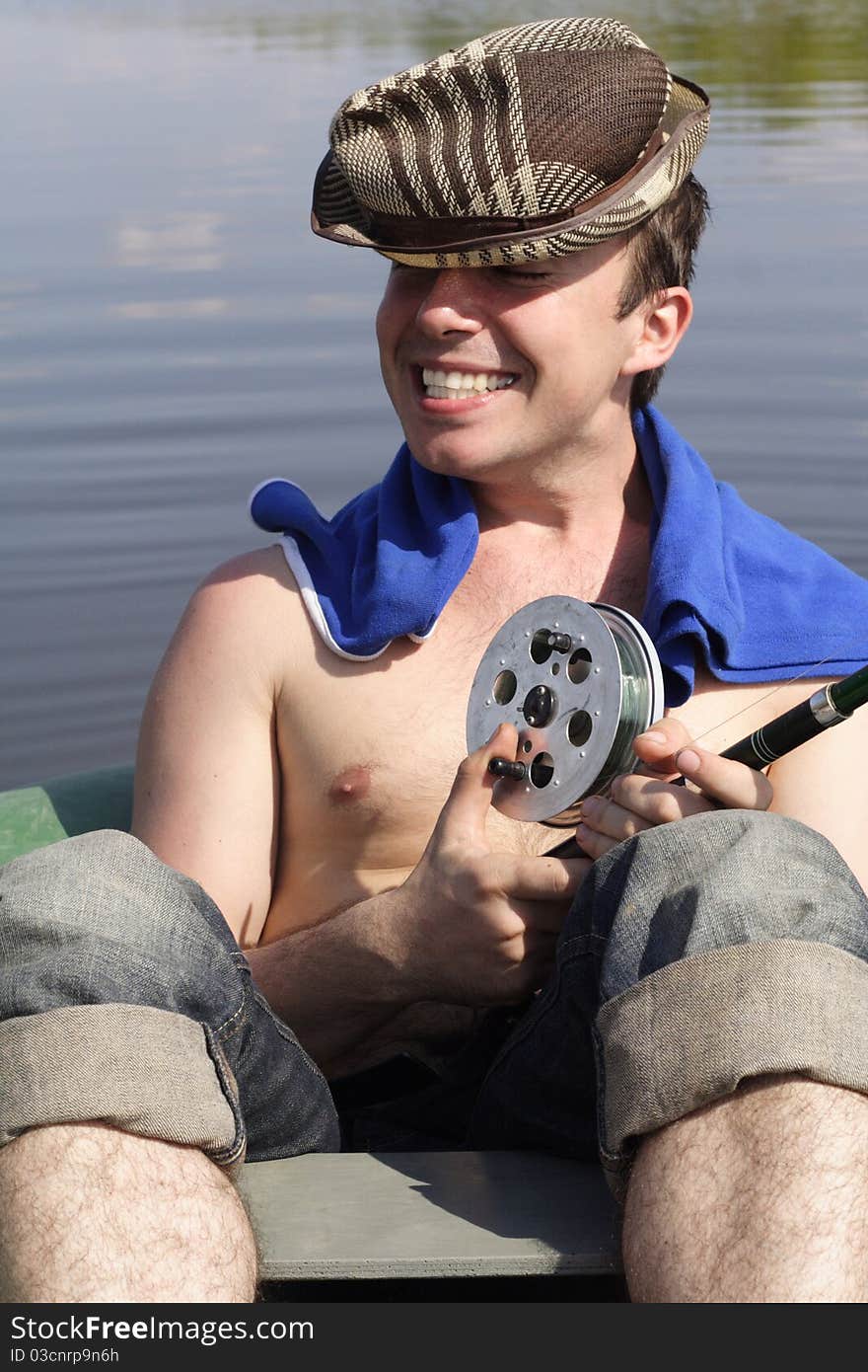 The young man sits in a boat with a spinning and smiles. The young man sits in a boat with a spinning and smiles