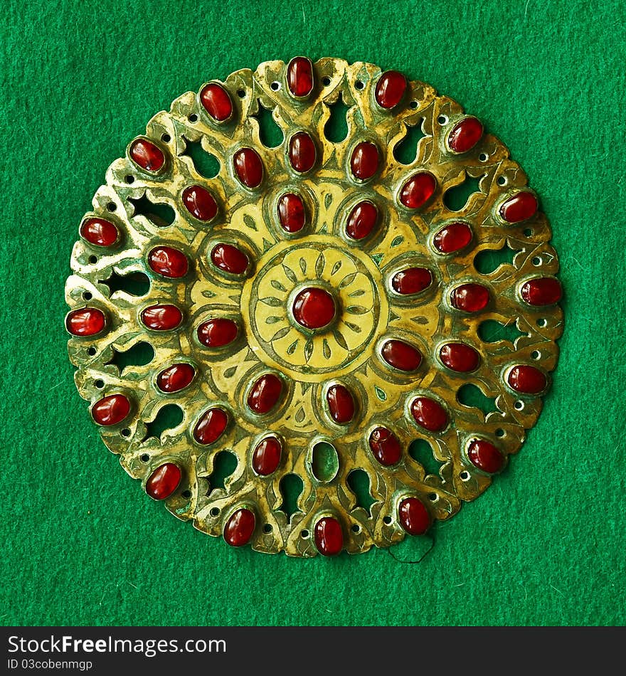 Middle-Asian vintage buckle for east dressing gown. Silver, gilding, semi-precious stones, east ornament. Isolated on dark green woollen cloth. Middle-Asian vintage buckle for east dressing gown. Silver, gilding, semi-precious stones, east ornament. Isolated on dark green woollen cloth.