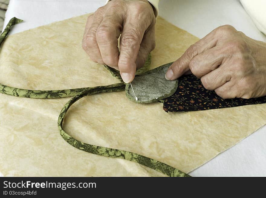 A quilter applies fabric glue to a leaf made of fabric for applique to background foundation. A quilter applies fabric glue to a leaf made of fabric for applique to background foundation.