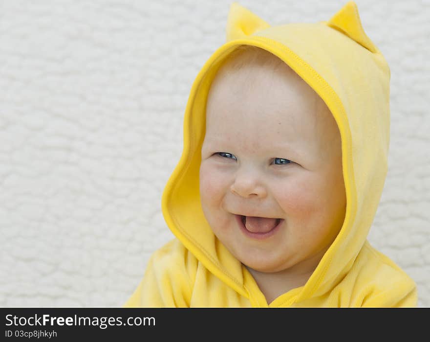 Portrait of the little girl (6 months) in a yellow hood which smiles on a light background. Portrait of the little girl (6 months) in a yellow hood which smiles on a light background