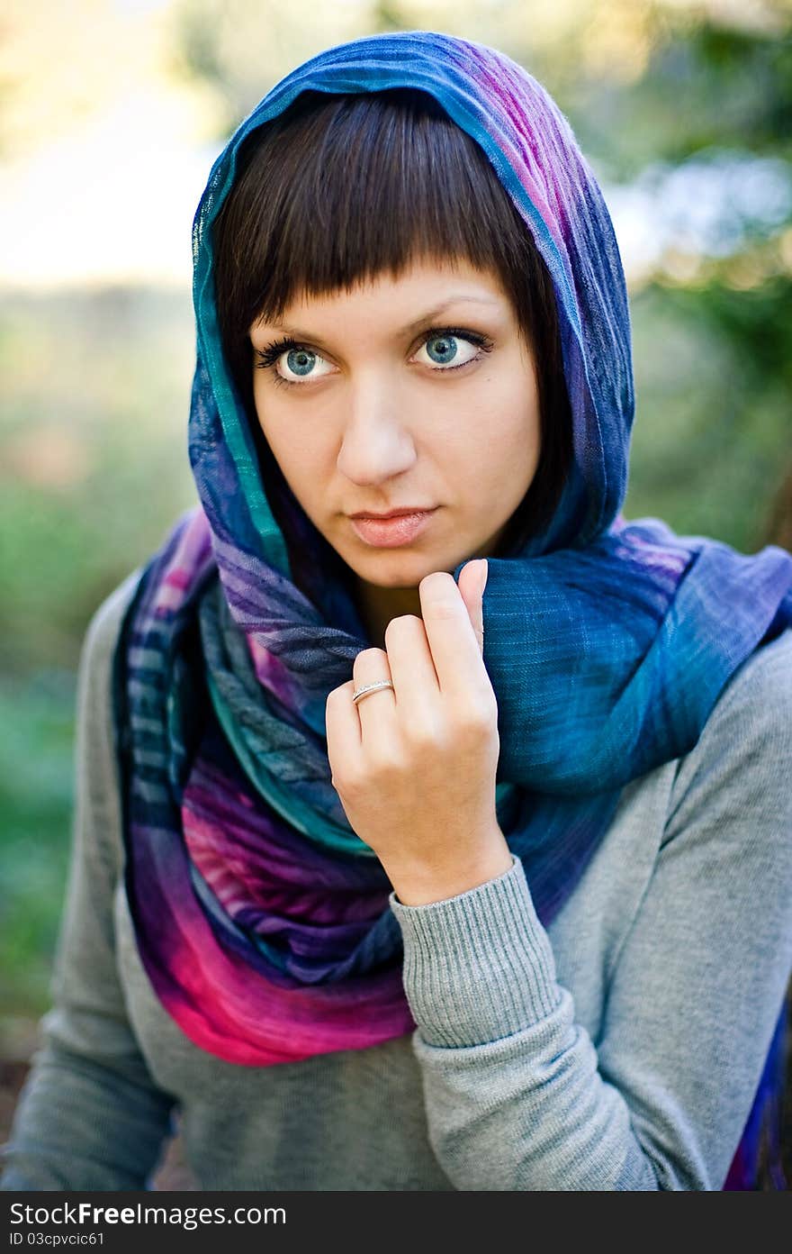 The girl in a scarf and in a knitted dress sits on a tree.