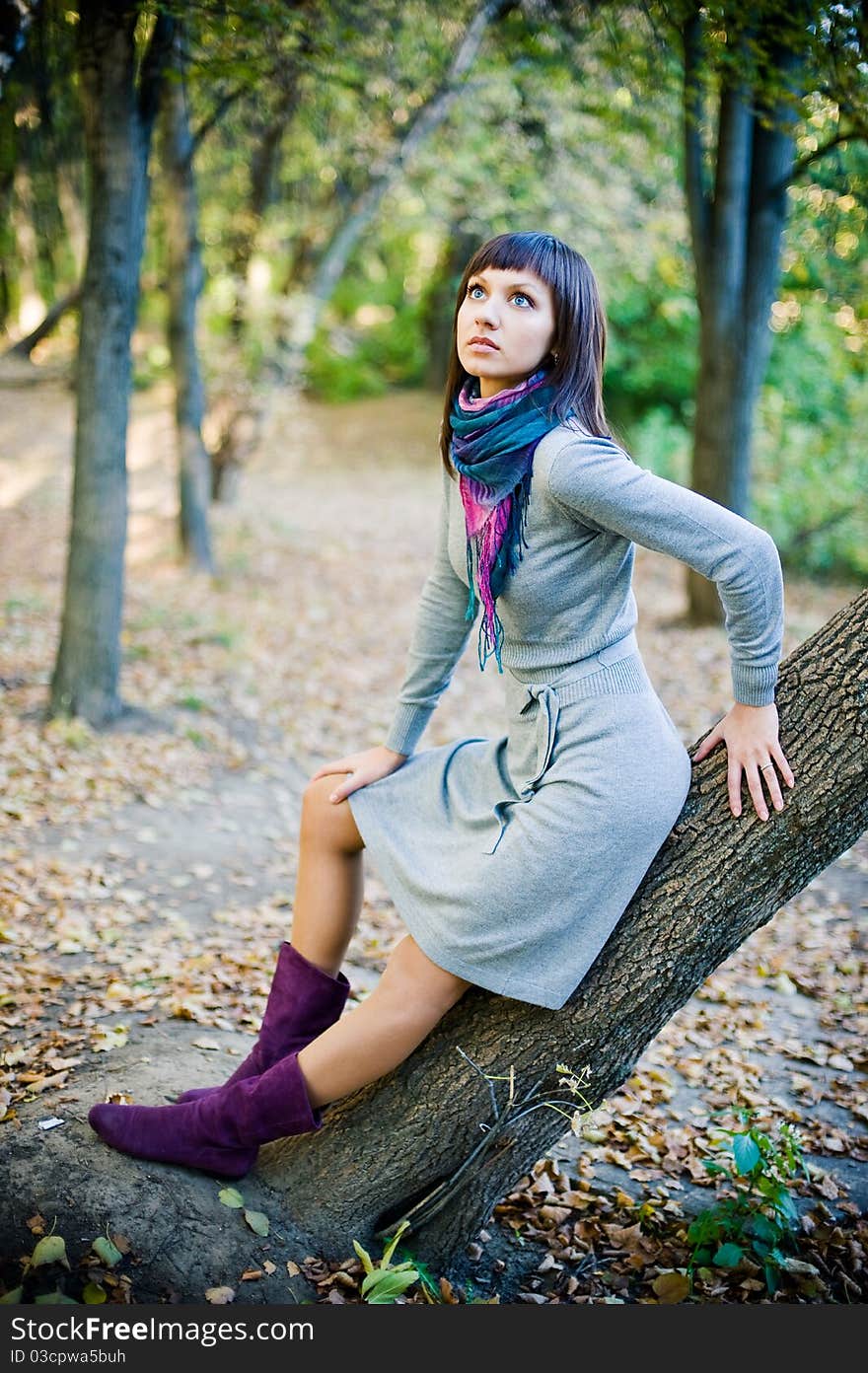 The girl in a scarf and in a knitted dress sits on a tree.