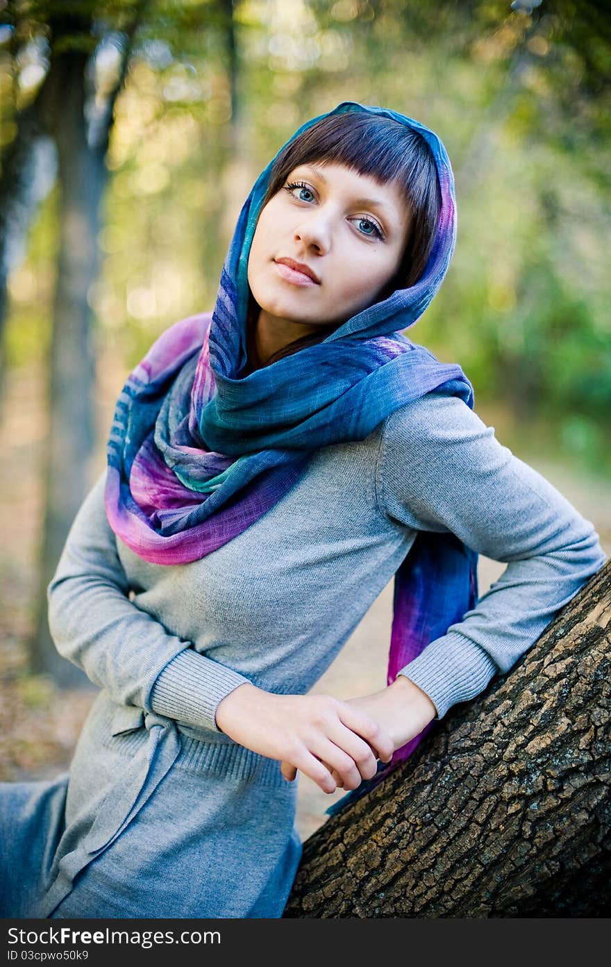 The girl in a scarf and in a knitted dress sits on a tree.