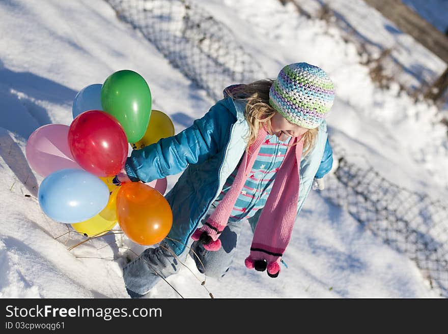 Young girl in a field of snow playing around with some balloons.