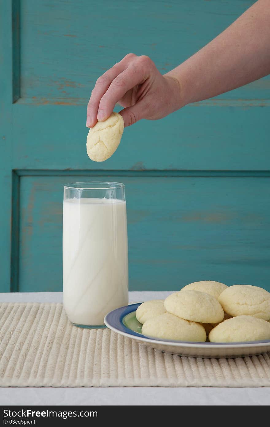 Hand ready to plunge a sugar cookie into a glass of milk. Hand ready to plunge a sugar cookie into a glass of milk