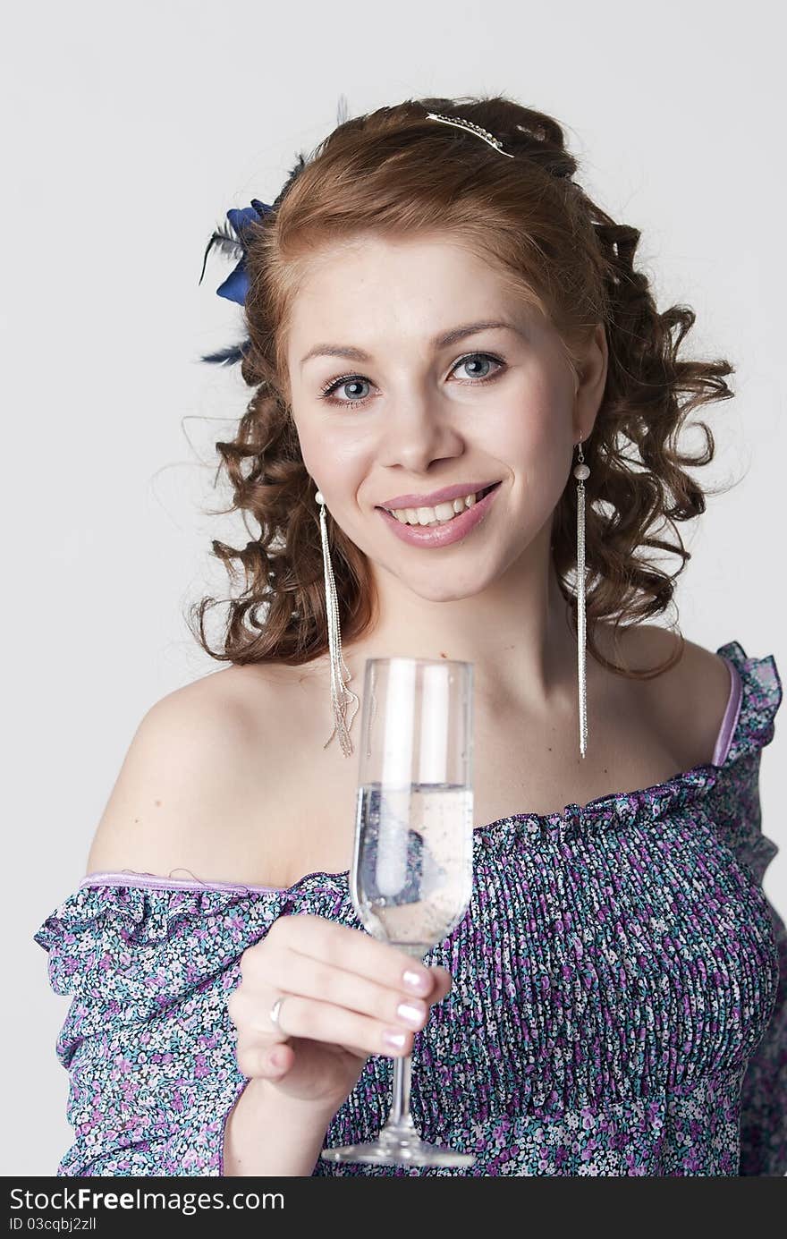 The young beautiful girl has control over a glass of water and smiles on a light background