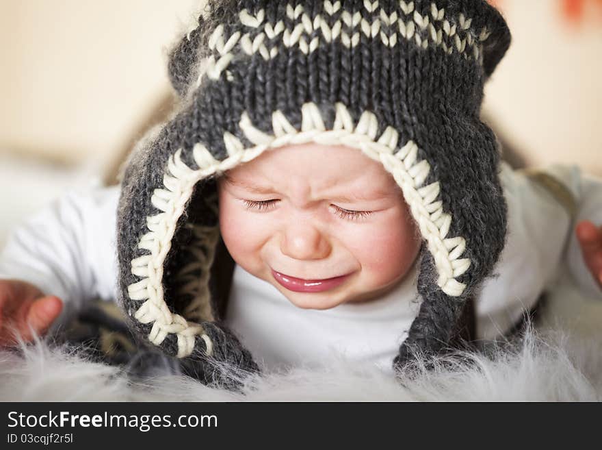 Close up portrait of sweet crying caucasian baby boy with grey cap lying on floor and looking down. Close up portrait of sweet crying caucasian baby boy with grey cap lying on floor and looking down.