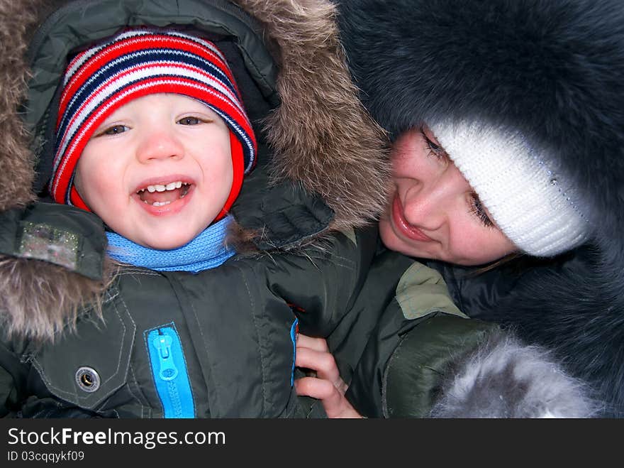 In the winter mother holds on hands of the laughing child in winter clothes. In the winter mother holds on hands of the laughing child in winter clothes