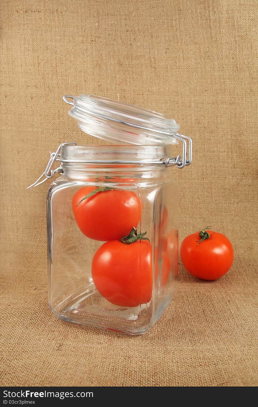 Red tomatoes in jar on jute background