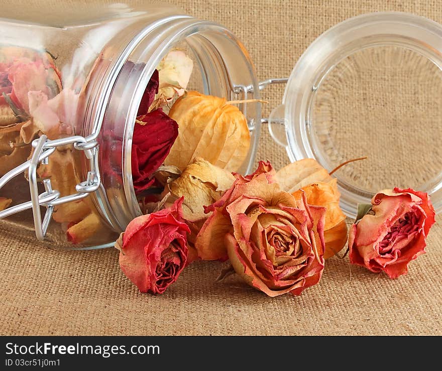 Buds of dry roses in glass bottle on jute background