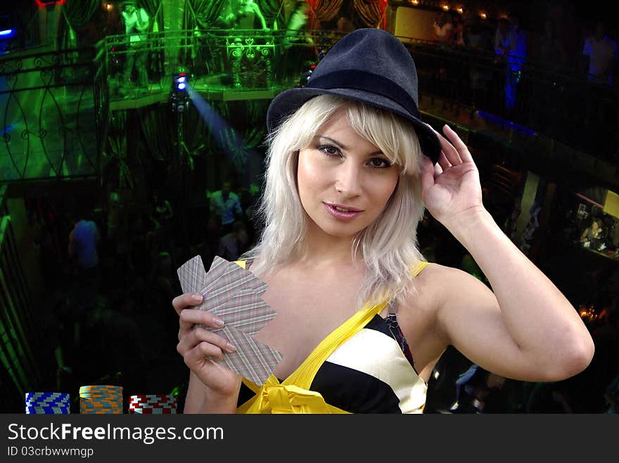 Blonde touching hat with cards in a hand looking intriguingly. Blonde touching hat with cards in a hand looking intriguingly