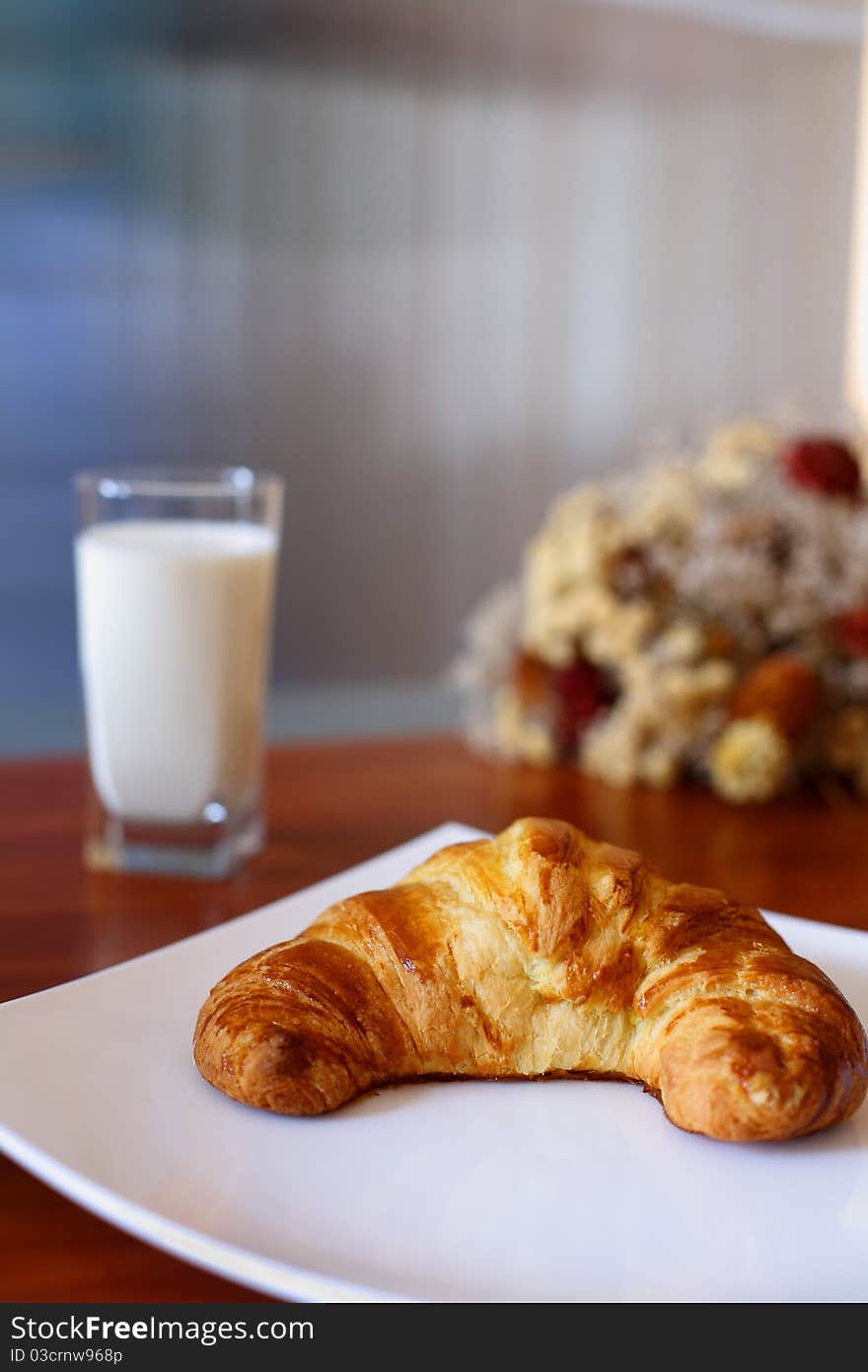 Appetizing croissant on a white plate and glass of milk