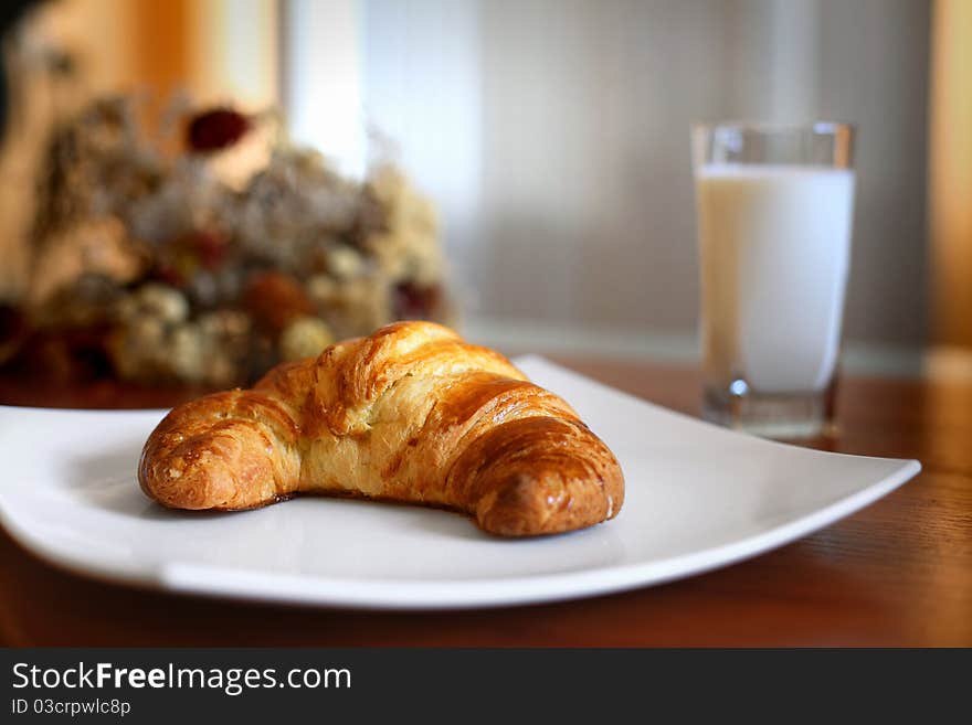 Appetizing croissant on a white plate and glass of milk