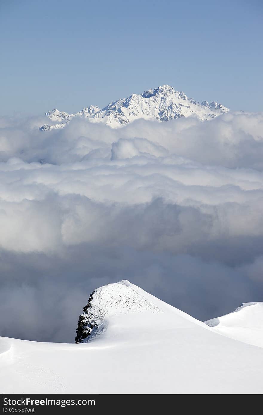 High snowy peaks over a grey cloud sea. High snowy peaks over a grey cloud sea