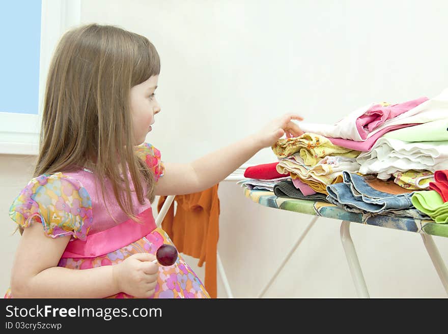 The girl in a beautiful dress costs near an ironing table and chooses things. The girl in a beautiful dress costs near an ironing table and chooses things