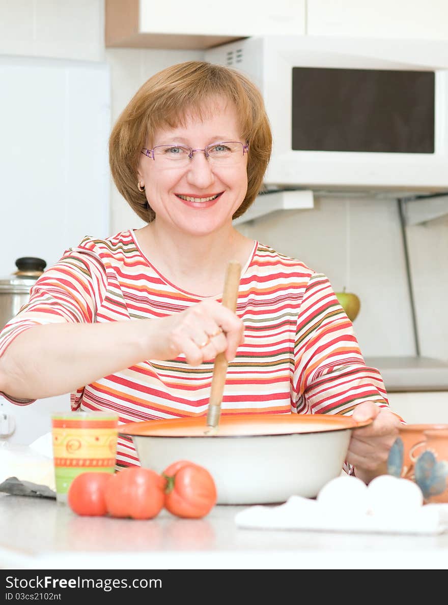 Joyful woman making dough in the kitchen at home