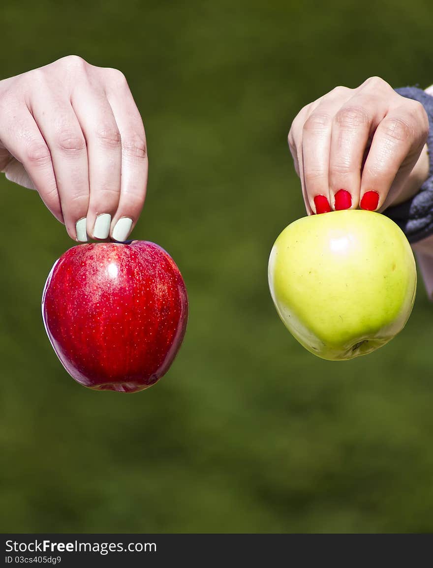 Two different hands holding two different apples in green background. Two different hands holding two different apples in green background