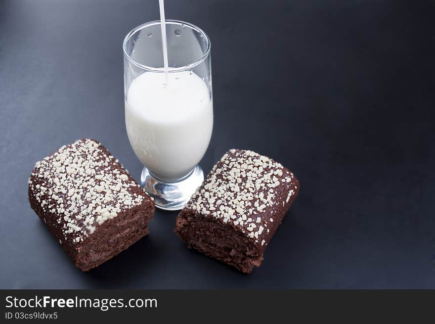 Chocolate roll and a glass of milk on a black background