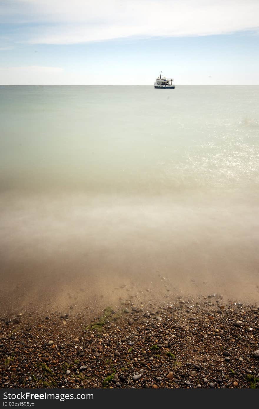 A long exposure day time wide angle photograph of the lake Ontario shore, with warm colors, and a ship at the horizon line. A long exposure day time wide angle photograph of the lake Ontario shore, with warm colors, and a ship at the horizon line.