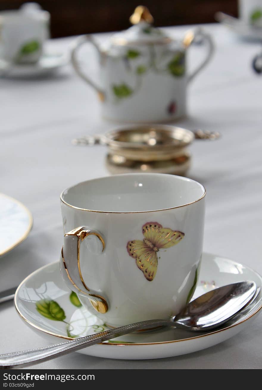 A teacup and saucer with spoon are in the foreground with other pieces in the background. A teacup and saucer with spoon are in the foreground with other pieces in the background.