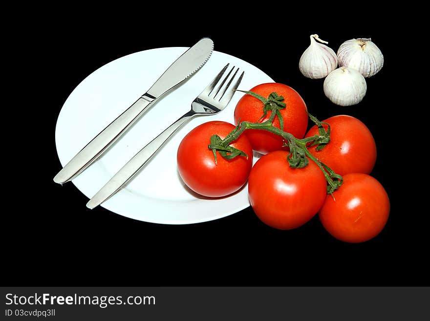 A Knife and Fork on a plate with tomato and garlic arranged. A Knife and Fork on a plate with tomato and garlic arranged