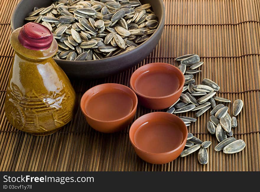 Chinese antique wine bottle with wine cups and sunflower seeds on brown bamboo table mat. Chinese antique wine bottle with wine cups and sunflower seeds on brown bamboo table mat.