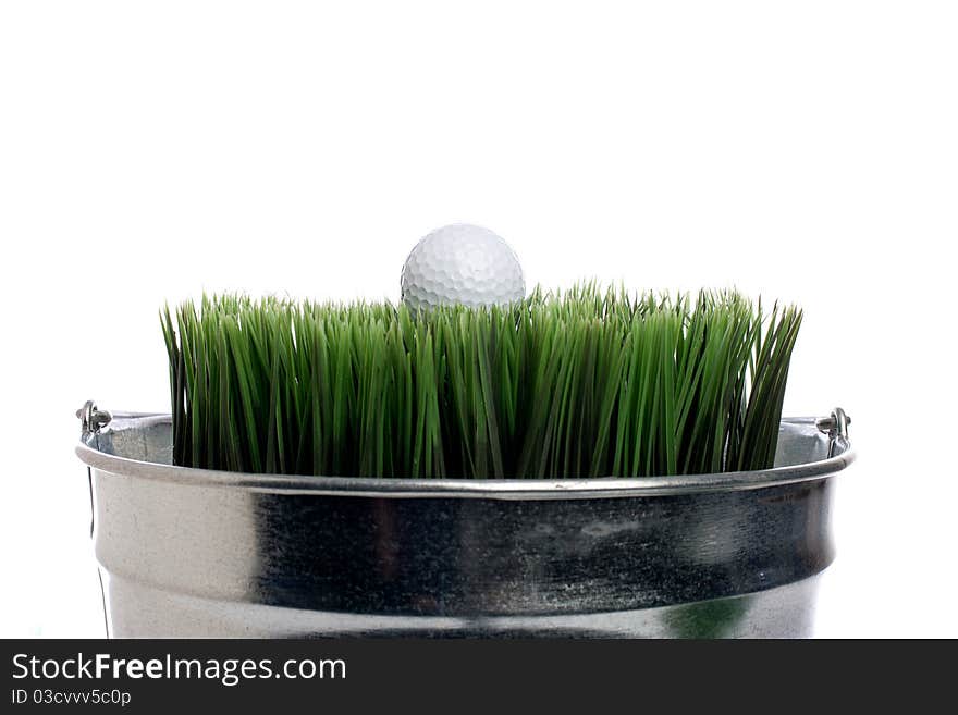 Horizontal image of a golf ball on grass in a small container on white. Container gardening