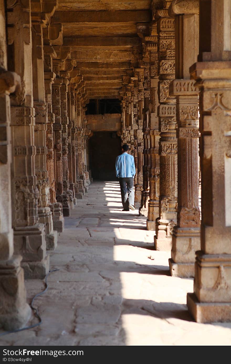 A man walking along an array of carved columns