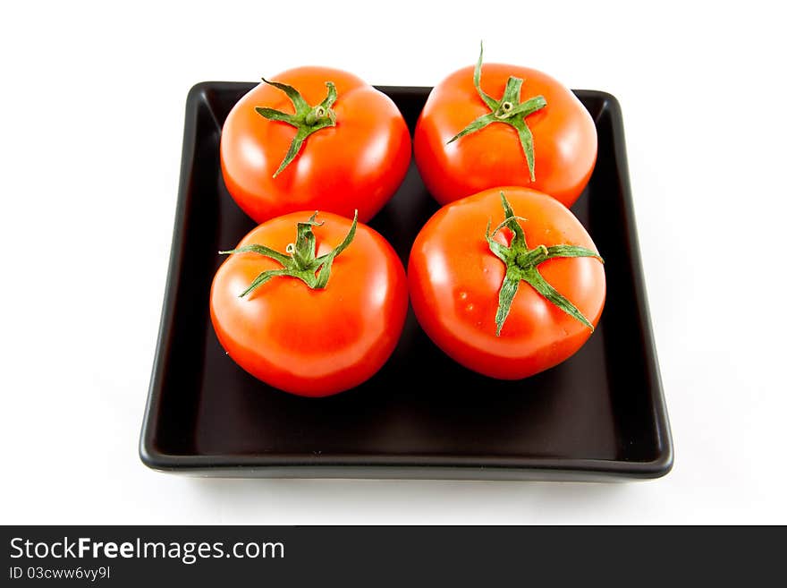 Four tomatoes on a black plate