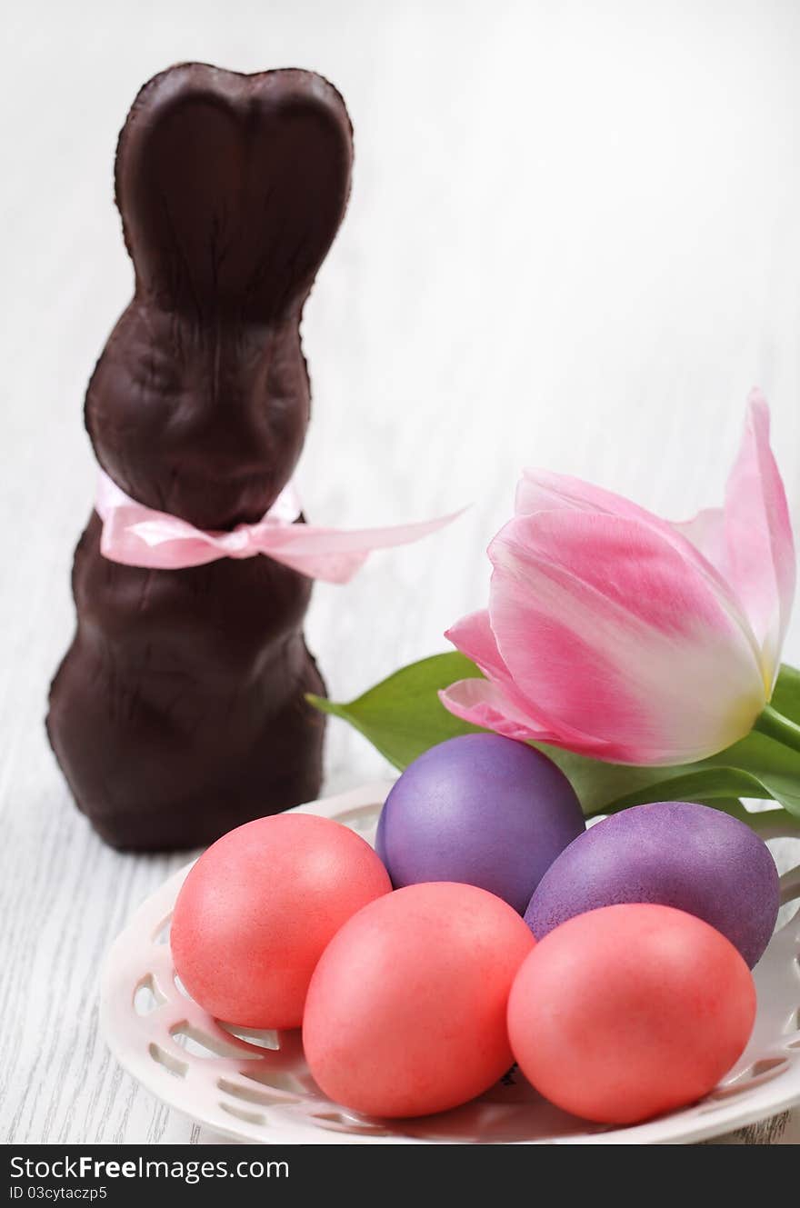 Easter eggs with tulip and chocolate hare on wooden background with space for text