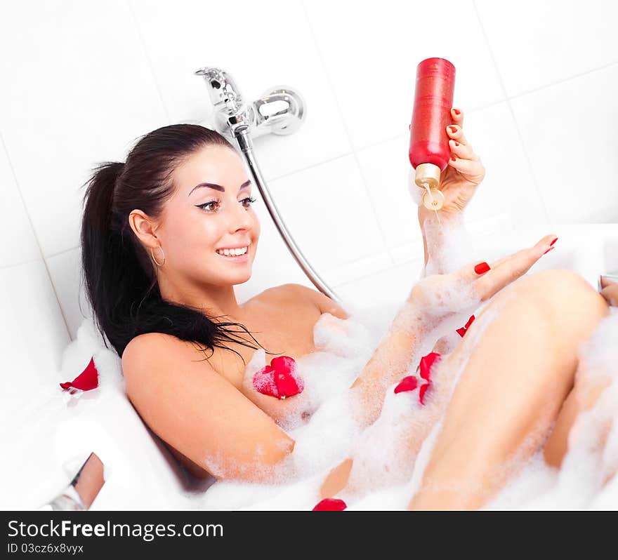 Beautiful young brunette woman taking a relaxing bath with foam and using shower gel. Beautiful young brunette woman taking a relaxing bath with foam and using shower gel