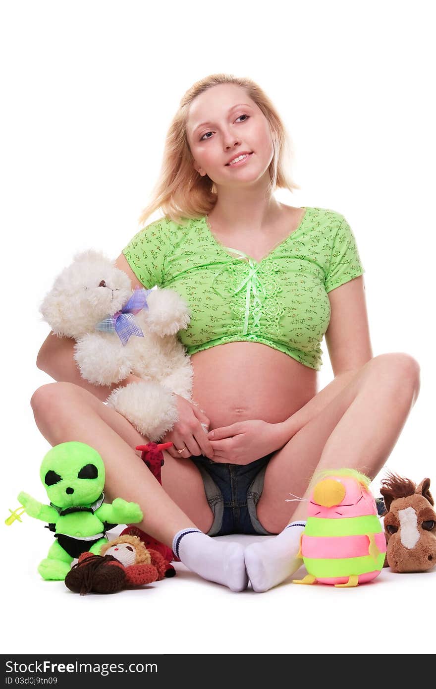 Cute pregnant girl, seated, surrounded by toys