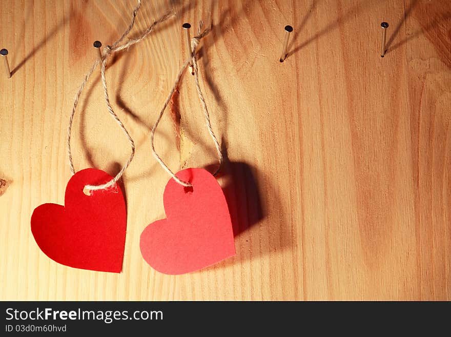 Two red paper hearts hanging on wooden wall with nails and ropes. Two red paper hearts hanging on wooden wall with nails and ropes