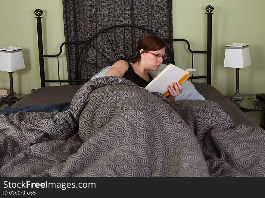 A young woman reads a book in bed. A young woman reads a book in bed