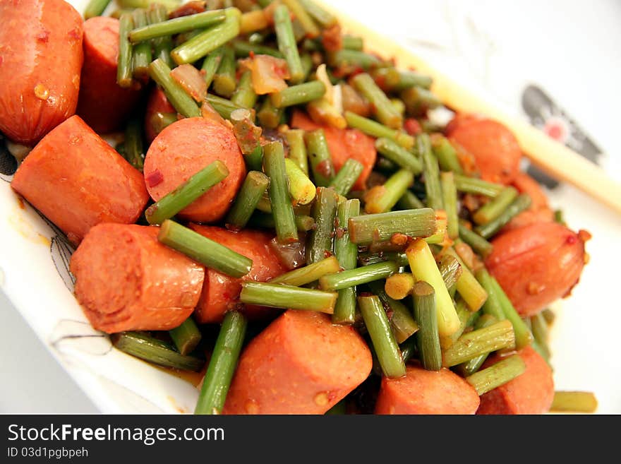 A fusion dish shot on white background: garlic sprouts and wieners. A fusion dish shot on white background: garlic sprouts and wieners.