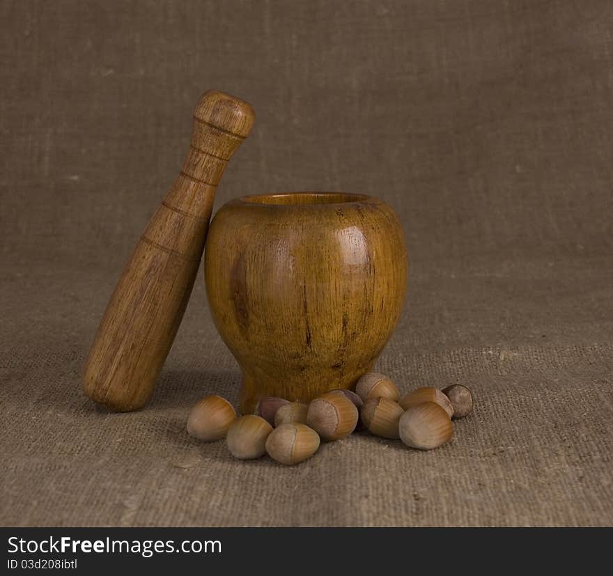 Wooden mortar and pestle with nuts on brown canvas